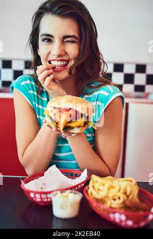 Je mange très bien. Portrait court d'une jeune femme attrayante qui apprécie un hamburger dans un restaurant rétro. Banque D'Images