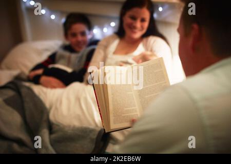 C'est une famille qui partage un amour de la lecture. Plan court d'un père lisant une histoire de coucher à sa femme et son fils. Banque D'Images