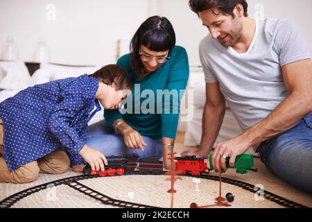 Montrant à ses parents comment accrocher le train. Photo d'une jeune famille qui a installé un train de jouets. Banque D'Images