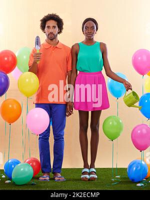 On se sent un peu à l'extérieur Un couple africain embarrassant entouré de ballons colorés tout en tenant les mains. Banque D'Images