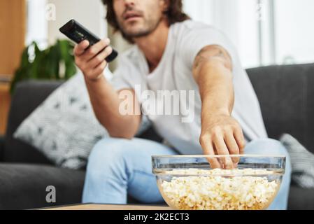 Je pouvais manger tout ce bol sans que personne ne regarde. Coup de feu d'homme assis sur le canapé en train de manger du pop-corn et de regarder la télévision. Banque D'Images