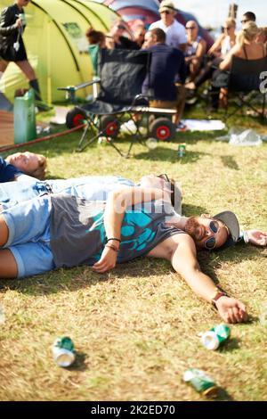 Quand les bons moments passent mal. Photo d'un groupe de gars passa sur l'herbe entourée de canettes de bière vides lors d'un festival en plein air. Banque D'Images