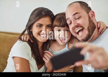 Super heureux de passer du temps avec la famille. Photo d'une mère et d'un père prenant des selfies avec leur jeune fille à la maison. Banque D'Images