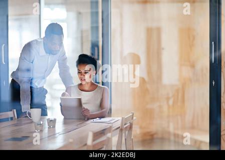 Ils mettent toujours les heures en place. Prise de vue de deux collègues utilisant une tablette numérique dans un bureau. Banque D'Images