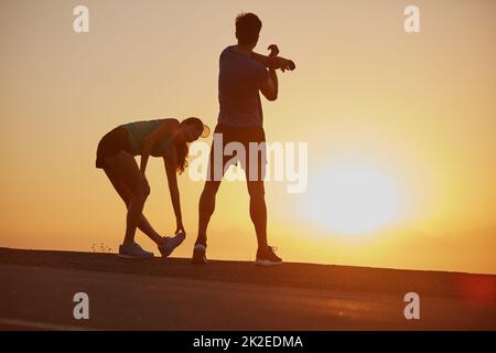 Sentir la brûlure et l'aimer. Photo d'un couple silhoueté pour une course au lever du soleil. Banque D'Images