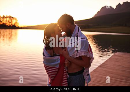 Juste nous deux Photo d'un jeune couple affectueux en maillots de bain enveloppés d'une serviette sur un lac. Banque D'Images