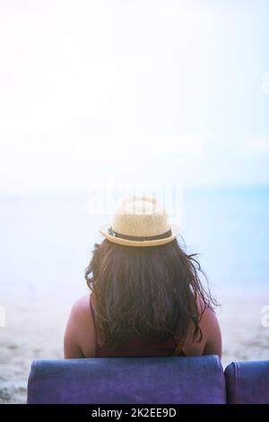 Prendre la vue. Vue arrière d'une jeune femme assise sur une chaise à la plage. Banque D'Images