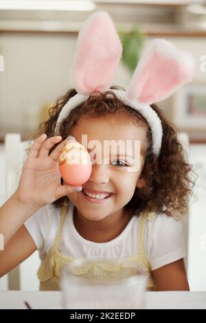 Montrant mon art. Photo d'une petite fille couvrant son œil avec un œuf de Pâques peint. Banque D'Images