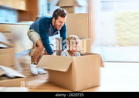 Nous allons dans le vaisseau spatial. Prise de vue d'un jeune homme joyeux qui pousse son fils dans une boîte imaginant sa voiture à l'intérieur à la maison pendant la journée. Banque D'Images