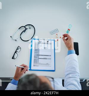 Définir le meilleur plan de traitement pour ses patients. Prise de vue en grand angle d'un médecin méconnaissable occupé par la paperasserie et les médicaments dans son bureau. Banque D'Images