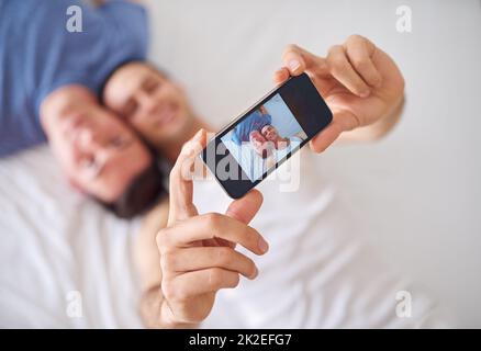 Immortalisez un moment d'amour. Photo d'un jeune couple gay prenant un selfie tout en se relaxant au lit. Banque D'Images