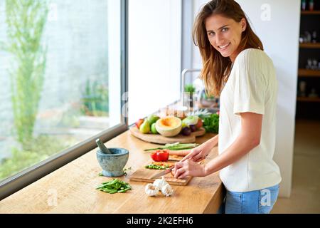 La cuisine est mon bonheur. Prise de vue d'une jeune femme attirante hacher des légumes dans une cuisine. Banque D'Images