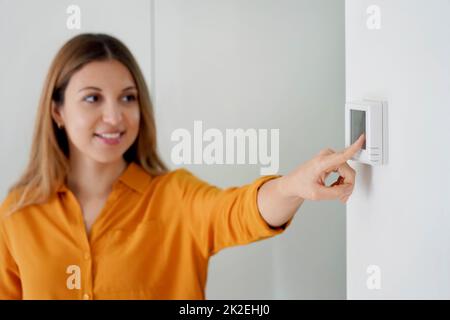 Une jeune femme abaisse la température pour économiser de l'énergie. Jeune fille réglant le thermostat de chauffage central numérique à la maison. Concentrez-vous sur la main. Banque D'Images