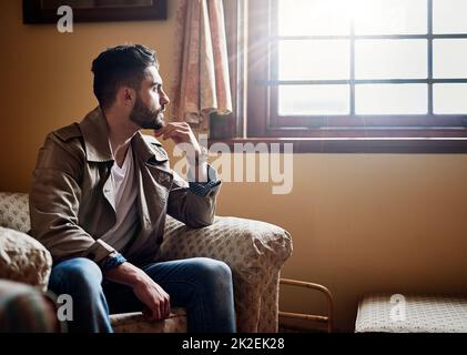 Réfléchir à Photo d'un beau jeune homme profondément réfléchi tout en étant assis sur une chaise à la maison. Banque D'Images