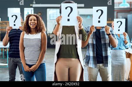 Il ne remet pas en question ma position dans cette entreprise. Portrait d'une jeune femme d'affaires debout parmi ses collègues tenant des plaques avec des points d'interrogation dans un bureau. Banque D'Images