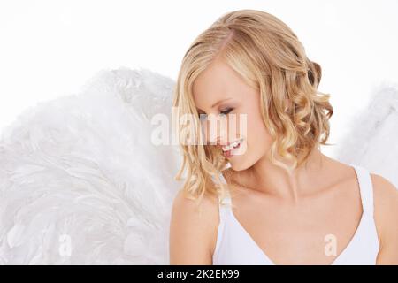 Sa beauté est lumineuse. Photo studio d'une jeune femme dans des ailes d'ange isolées sur blanc. Banque D'Images