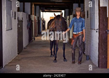 Vous vous en sortez pour prendre un hors-la-loi. Photo d'une cowgirl menant un cheval hors d'une écurie. Banque D'Images