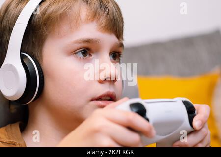 Portrait d'un jeune garçon concentré avec un joystick dans ses mains jouant la console. Banque D'Images