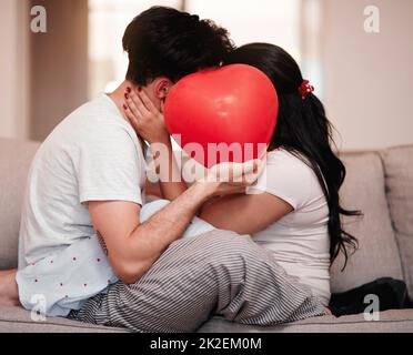 L'amour est la raison. Photo courte d'un jeune couple méconnaissable embrassant derrière un ballon en forme de cœur le jour de la Saint-Valentin. Banque D'Images