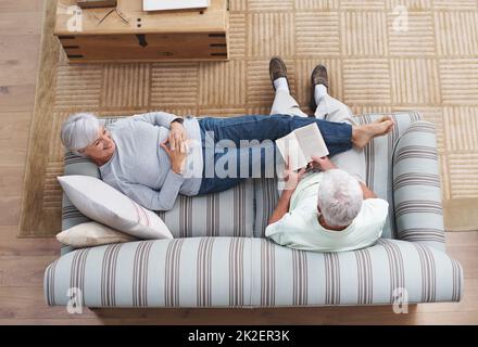 La poésie est le langage de l'amour Un homme âgé lisant à sa femme comme elle se trouve sur le canapé. Banque D'Images