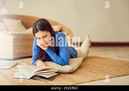 Vraiment engrosé dans le récit. Photo d'une jeune femme lisant un livre sur son salon à la maison. Banque D'Images