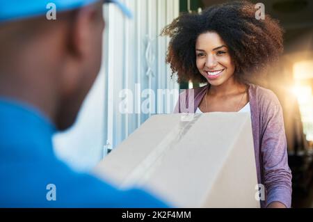 Il est arrivé plus tôt que nous l'espérions. Photo d'un employé des postes livrant un colis à une jeune femme cliente. Banque D'Images