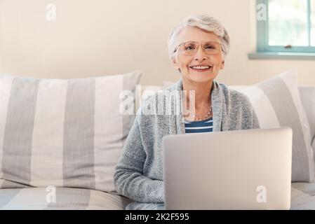 De loin le moyen le plus simple de rester à jour. Photo d'une femme âgée utilisant un ordinateur portable sur le canapé à la maison. Banque D'Images