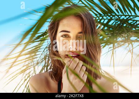 Oh, quel été magnifique. Photo d'une jeune femme attrayante debout sous l'ombre d'un palmier à la plage. Banque D'Images