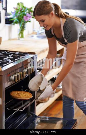 Cuit à la perfection. Photo d'une jeune femme attirante qui sort une tarte du four. Banque D'Images