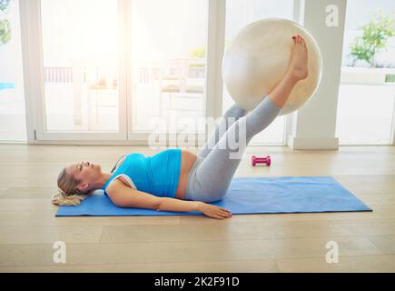 Rester en suspens pendant son dernier trimestre. Prise de vue d'une femme enceinte travaillant avec une balle d'exercice à la maison. Banque D'Images