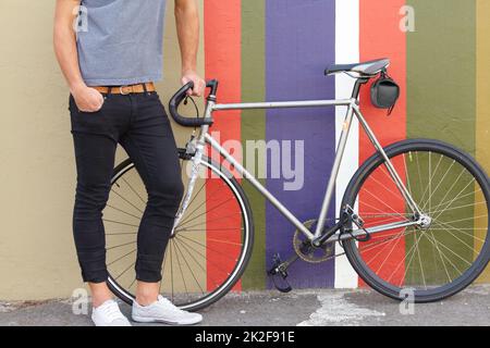 Aimez-vous ma course ? Photo courte d'un jeune homme habillé avec élégance et debout à côté d'un vélo sur un fond coloré. Banque D'Images