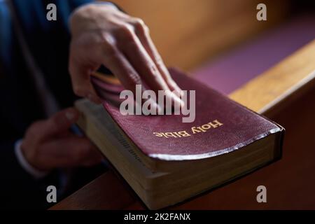 Trouver le confort dans le bon livre. Plan court d'un homme ouvrant une bible tout en étant assis dans un pew à l'église. Banque D'Images