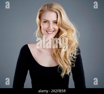 Cheveux aussi lumineux que le soleil. Studio portrait d'une jeune femme attrayante avec de beaux cheveux blond longs posant sur un fond gris. Banque D'Images