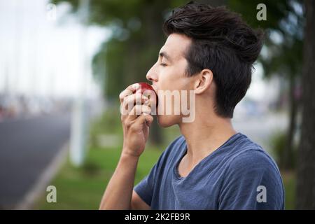 Prendre un morceau. Un jeune homme prenant une piqûre de pomme en attendant le bus. Banque D'Images