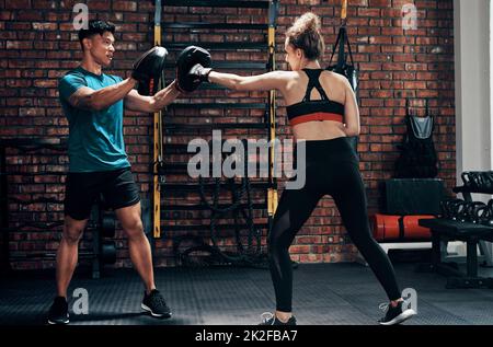 Sa technique de poinçonnage est incroyable. Coupe courte d'un joli boxer féminin s'entraîner avec son entraîneur personnel dans une salle de sport. Banque D'Images