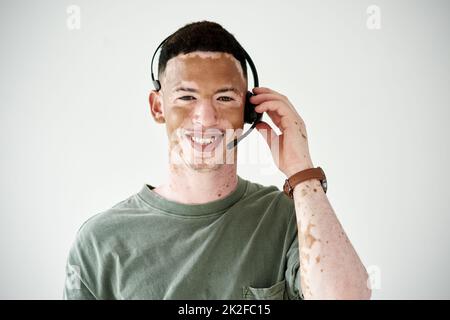 ID soyez heureux de vous parler de nos offres. Portrait studio d'un jeune homme avec vitiligo portant un casque sur fond blanc. Banque D'Images