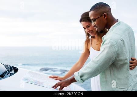 Le vrai amour ne vous conduit jamais à vous égarer. Photo d'un jeune couple heureux lisant une carte sur une route le long de la côte. Banque D'Images