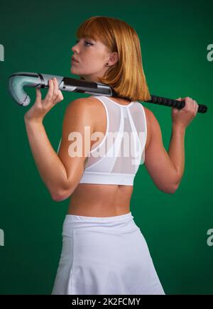 Je suis toujours au top de mon jeu. Plan court d'un jeune sportif attrayant debout seul et posant avec un bâton de hockey sur un fond de studio vert. Banque D'Images