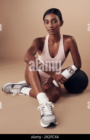 Confiance et objectifs du corps combinés. Prise de vue en longueur d'une jeune femme attrayante assise seule et posant dans le studio après son entraînement. Banque D'Images