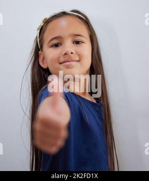 Parfois, nous avons juste besoin d'un peu d'encouragement. Photo d'une adorable petite fille montrant les pouces vers le haut tout en posant contre un mur. Banque D'Images