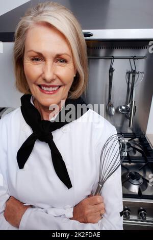 Chef féminin tenant un fouet en fil devant un poêle à gaz. Portrait en gros plan d'une femme chef tenant un fouet métallique debout devant un poêle à gaz. Banque D'Images