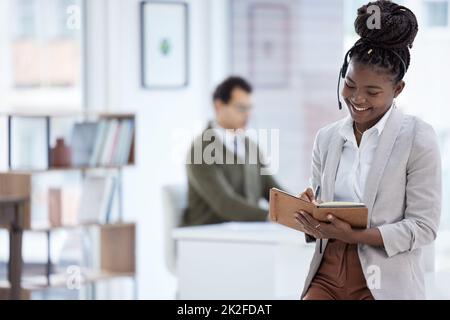 En tenant compte des résultats des ventes. Photo d'une jeune femme d'affaires portant un casque et écrivant des notes pendant son travail au bureau. Banque D'Images