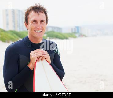 Vous vous sentez bien après une session épique. Un surfeur posant sur la plage avec sa planche à côté du copyspace. Banque D'Images