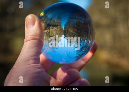 Main tenant une boule de verre avec une image de nature et de paysage inversées Banque D'Images