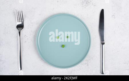 Trois petits pois verts sur une assiette, fourchette et couteau sur la table, régime et concept de perte de poids, mode de vie sain Banque D'Images