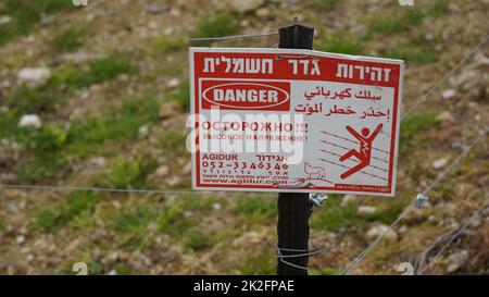 Panneau d'avertissement de danger de clôture électrique. Écrit en trois langues - hébreu, russe, anglais. Avertissement de mort Banque D'Images