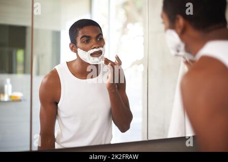 Se débarrasser des poils tenaces. Un jeune homme se raser dans le miroir. Banque D'Images