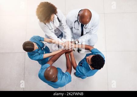 C'est parti pour la journée. Prise de vue en grand angle d'un groupe de jeunes médecins formant un caucus avec leurs mains à l'intérieur d'un hôpital pendant la journée. Banque D'Images