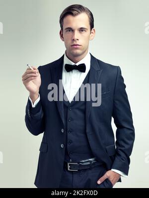 Suave et sophistiqué. Un portrait en studio d'un jeune homme confiant fumant une cigarette. Banque D'Images