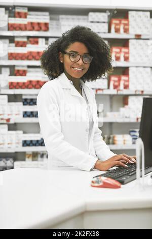 Nous faisons aussi des réservations. Portrait d'une jeune pharmacienne gaie qui tape sur un ordinateur tout en regardant l'appareil photo. Banque D'Images